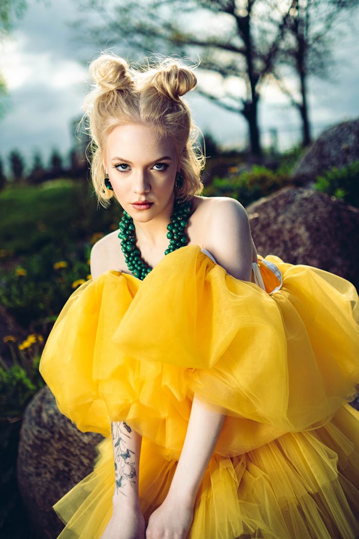 Elegant woman in a bright yellow dress poses outdoors, showcasing fashion and style.